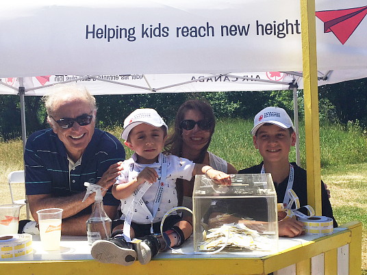 Calin Rovinescu, président et chef de la direction d’Air Canada, Kaleb, la maman de Kaleb, ainsi que Justin au kiosque de limonade du septième tournoi de golf annuel de la Fondation Air Canada. (Groupe CNW/Fondation Air Canada)